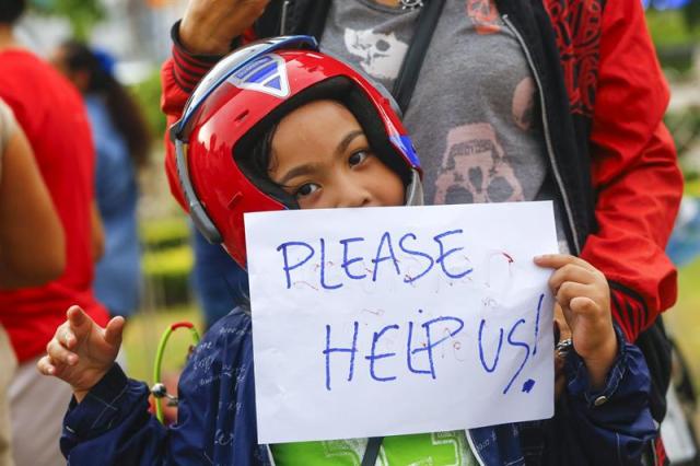 Un niño con un carte que pone "Por favor ayudenos" se manifiesta en el monumento de la Victoria en contra del golpe de estado en Bangkok, Tailandia hoy 27 de mayo de 2014. La economía de Tailandia, desgastada por meses de manifestaciones en las calles, ha recibido una nueva carga con el golpe de Estado dado por el Ejército el pasado día 22 sin un calendario claro para el restablecimiento de la normalidad. EFE/Diego Azubel