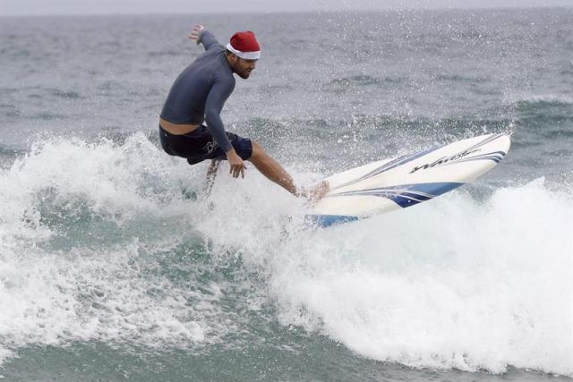 El surfista Guy Miller toma una ola con su tabla durante la tradicional celebración de Navidad en la playa de Bondi Beach de Sídney (Australia), hoy, 25 de diciembre de 2014. Familias y turistas se reúnen cada año en esta playa para conmemorar el día de Navidad, que coincide en pleno verano australiano. EFE/Dean Lewins PROHIBIDO SU USO EN AUSTRALIA Y NUEVA ZELANDA