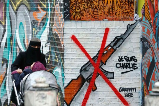 A woman pushes a pram past a "Je Suis Charlie" street art near Brick Lane in east London