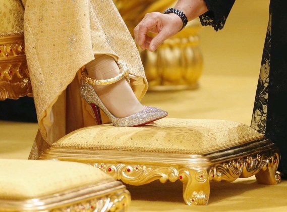 A lady-in-waiting adjusts the dress and Christian Louboutin shoes of Dayangku Raabi'atul 'Adawiyyah Pengiran Haji Bolkiah as Adawiyyah waits for Prince Abdul Malik to arrive for the enthronement ceremony at their wedding in Bandar Seri Begawan