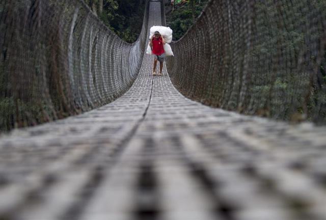 Un grangero nepalí traslada un fardo que contiene productos agrícolas mientras cruza una pasarela sobre el río Trishul en Nepal, hoy, 13 de abril de 2015. Granjeros nepalíes de la región atraviesan este puente colgante para abastecer con sus productos a los mercados de la zona. EFE/NARENDRA SHRESTHA