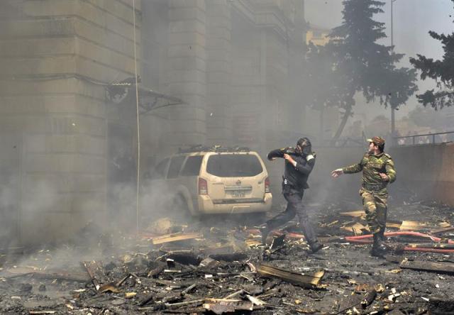 Dos policías corren escapando de los escombros que caen de un edificio de pisos incendiado en Bakú, Azerbaiyán, hoy, martes 19 de mayo de 2015. Al menos quince personas murieron hoy y 30 tuvieron que ser hospitalizadas a consecuencia de un incendio en un edificio de 16 plantas situado en el barrio de Binagadi, en el norte de la capital azerbaiyana, que los bomberos han tardado varias horas en sofocar. El fiscal general, Zakir Garálov, adelantó como posible causa del siniestro la mala calidad del revestimiento aislante del edificio, que fue donde se originó el fuego, según testigos. EFE/Orxan Azim