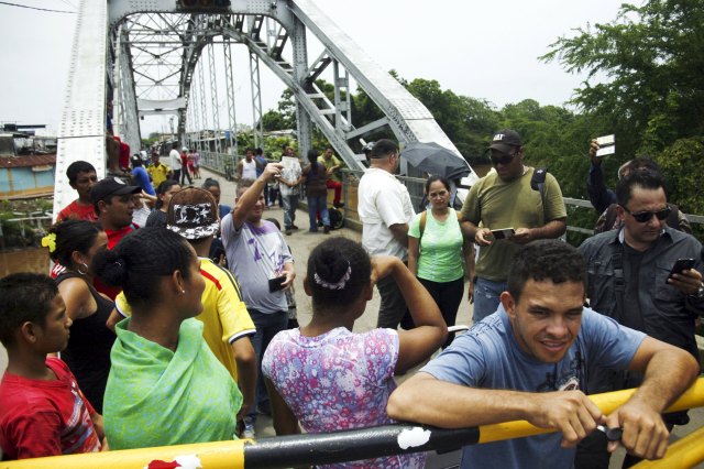 People stand next to a closed gate as they wait to try to cross La Union international bridge, on the border with Colombia at Boca de Grita in Tachira state, Venezuela