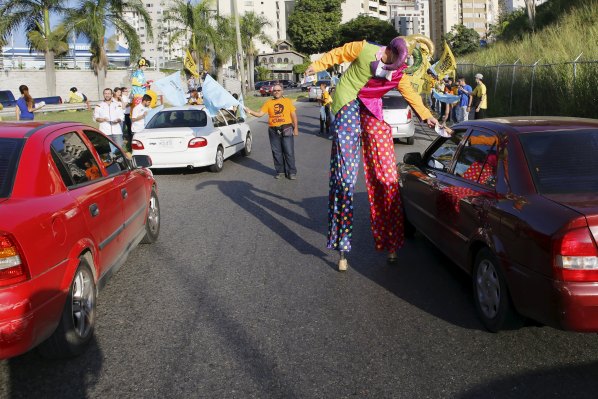 A man on a pair of stilts hands out a flyer to commuters as he campaigns for Venezuelan coalition of opposition parties Democratic Unity Roundtable (MUD) on a street in Caracas November 13, 2015. Venezuela will hold parliamentary elections on December 6. REUTERS/Marco BelloFOR EDITORIAL USE ONLY. NO RESALES. NO ARCHIVE.