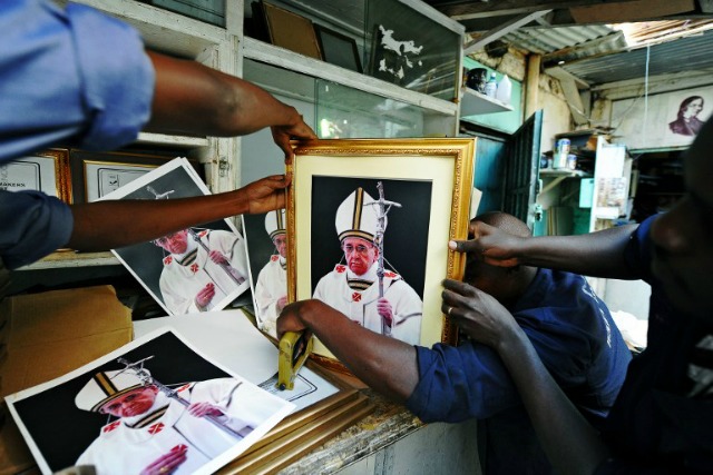 Los trabajadores pusieron los toques finales a los retratos enmarcados de Francisco en una línea de montaje de taller en Nairobi el 18 de noviembre de 2015. Francisco visitará Kenia, Uganda y la República Centroafricana del 25 de noviembre al 30 de noviembre de 2015. Kenya dijo que podría implementar como hasta 10.000 policías para aumentar la seguridad durante la visita del Papa, ya que el país se prepara para una multitud de un millón de personas. AFP PHOTO / JOHN MUCHUCHA