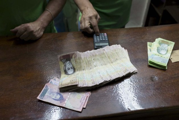 Men count Venezuelan bolivar notes, which they received for their work as carwashers during the week, at a parking lot in Caracas January 22, 2016. REUTERS/Marco Bello