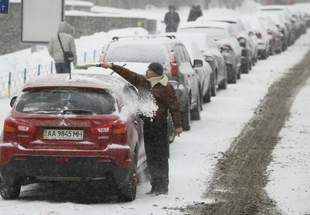 Un hombre limpia su coche después de una nevada en el centro de Kiev, Ucrania, 25 de enero de 2016. REUTERS / Gleb Garanich