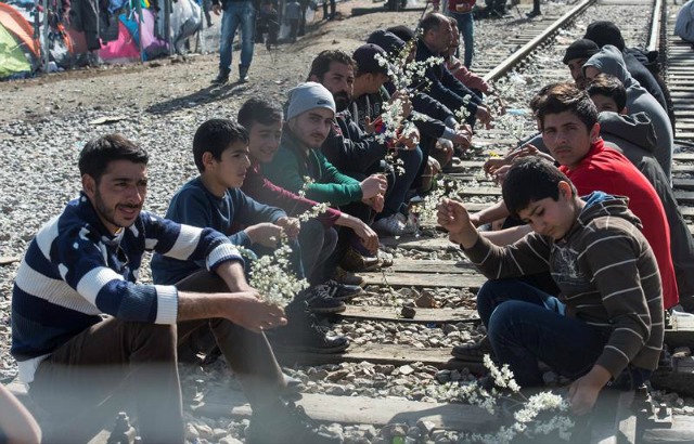 Varios refugiados sostienen ramos de flores mientras esperan en la parte griega poder cruzar a Macedonia, cerca de la localidad macedonia de Gevgelija, hoy, 1 de marzo de 2016. Unos 30.000 refugiados y migrantes están atrapados en estos momentos en Grecia a la espera de poder continuar su ruta hacia el norte de Europa, mientras que la frontera con Macedonia está herméticamente cerrada tras los incidentes registrados este lunes. EFE/Georgi Licovski