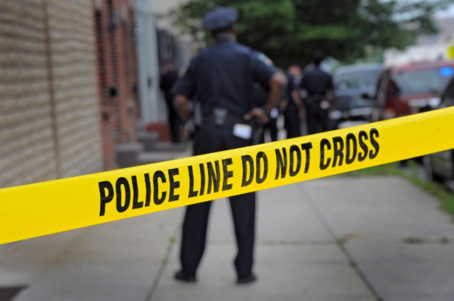 A Baltimore Police officer stands behind crime scene tape at the scene of a police-involved shooting following a dispatch for a burglary in progress, reported near S. Chester Street and Bank Street in southeast Baltimore. A suspect was shot, while another was taken into custody as investigators pore through evidence. (Karl Merton Ferron/Baltimore Sun)