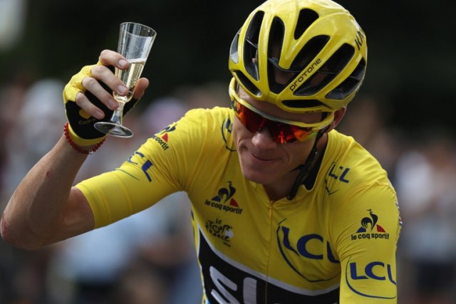 Great Britain's Christopher Froome, wearing the overall leader's yellow jersey, is handed a glass of champagne as he rides during the 113 km twenty-first and last stage of the 103rd edition of the Tour de France cycling race on July 24, 2016 between Chantilly and Paris Champs-Elysees.  / AFP PHOTO / KENZO TRIBOUILLARD