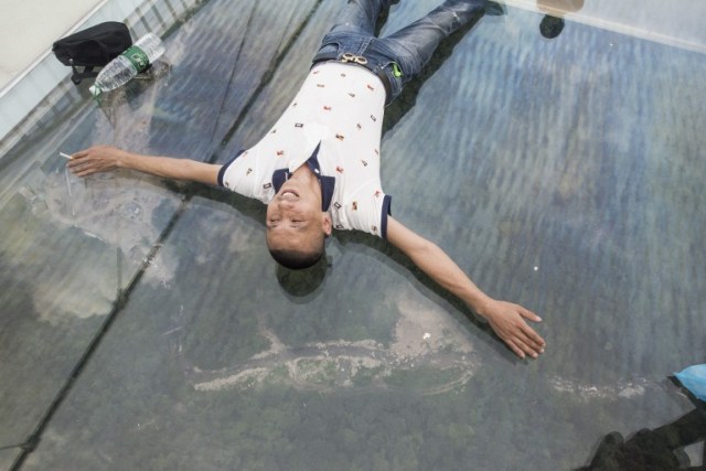 A tourist takes a photograph on the world's highest and longest glass-bottomed bridge above a valley in Zhangjiajie in China's Hunan Province on August 20, 2016. / AFP PHOTO / FRED DUFOUR