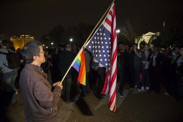 MHR36 WASHINGTON (EE.UU.), 09/11/2016.- Un hombre sostiene una bandera estadounidense del revés y una bandera arcoíris, símbolo del colectivo gay, frente a la Casa Blanca en Washington DC, Estados Unidos, hoy, 9 de noviembre de 2016. El candidato republicano, Donald Trump, ha ganado hoy las elecciones presidenciales en Estados Unidos y tomará posesión se su cargo en enero. EFE/Michael Reynolds