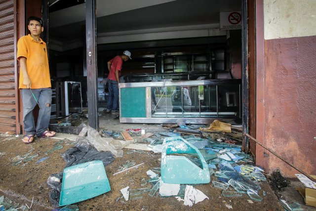 People stand next to broken glass as they look at the damage after a bakery was looted in Ciudad Bolivar, Venezuela December 17, 2016. REUTERS/William Urdaneta EDITORIAL USE ONLY. NO RESALES. NO ARCHIVE.