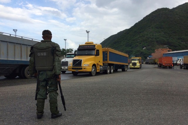 En esta imagen del 19 de diciembre de 2016, un soldado de la Guardia Nacional vigila camiones que salen del puerto en Puerto Cabello, Venezuela, la ciudad portuaria por la que pasan la mayoría de importaciones de alimentos del país. En toda la cadena de mando, de los generales de alto nivel a los soldados de a pie, los militares utilizan su creciente poder sobre el suministro de comida para lucrarse. (AP Foto/Ricardo Nunes)