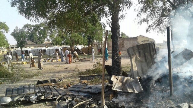 People walk at the site after a bombing attack of an internally displaced persons camp in Rann