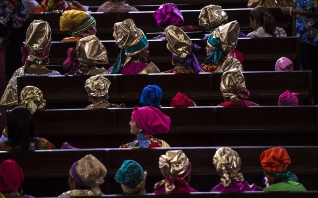 Women dressed as "madamas" attend a mass before the beginning of the Carnival in El Callao, Bolivar state, Venezuela on February 26, 2017. El Callao's carnival was recently named Unesco's Intangible Cultural Heritage of Humanity and is led by the madamas, the pillars of Callaoense identity representing Antillean matrons considered the communicators of values, who dance and wear colourful dresses. / AFP PHOTO / JUAN BARRETO