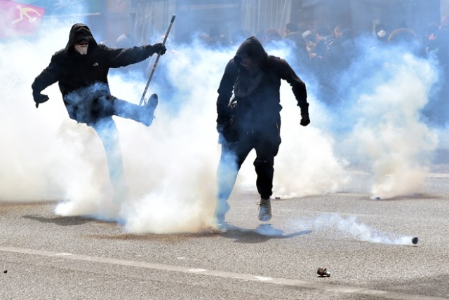 Demonstators take part in a march among fumes of smoke bombs during clashes taking place at a march for the annual May Day workers' rally in Paris on May 1, 2017. / AFP PHOTO / CHRISTOPHE ARCHAMBAULT