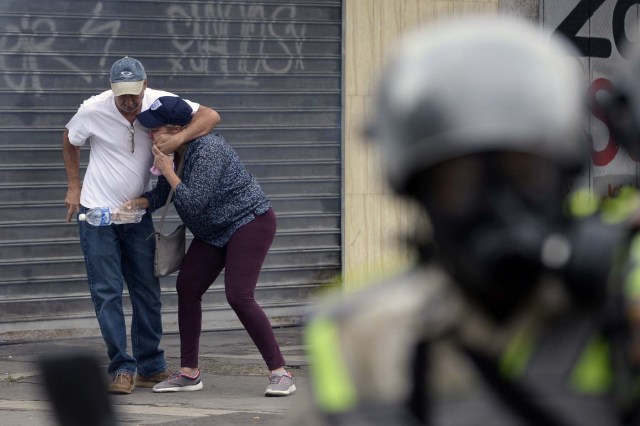 Venezuelan opposition activists protect themselves from tear gas shot by police during a march against President Nicolas Maduro, in Caracas on May 1, 2017. Security forces in riot vans blocked off central Caracas Monday as Venezuela braced for pro- and anti-government May Day protests one month after a wave of deadly political unrest erupted.  / AFP PHOTO / FEDERICO PARRA