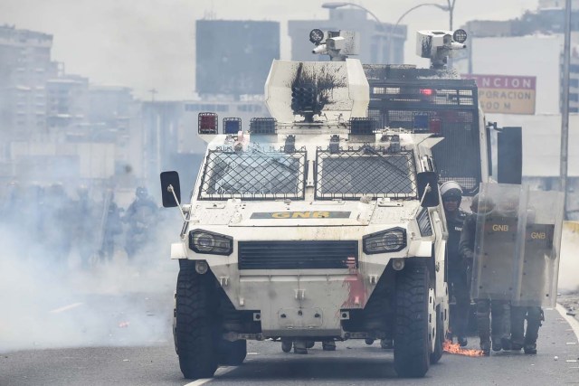 Riot police agents next to an armoured vehicle move forward along a blocked street, during clashes within a protest against Venezuelan President Nicolas Maduro, in Caracas on May 3, 2017. Venezuela's angry opposition rallied Wednesday vowing huge street protests against President Nicolas Maduro's plan to rewrite the constitution and accusing him of dodging elections to cling to power despite deadly unrest. / AFP PHOTO / JUAN BARRETO