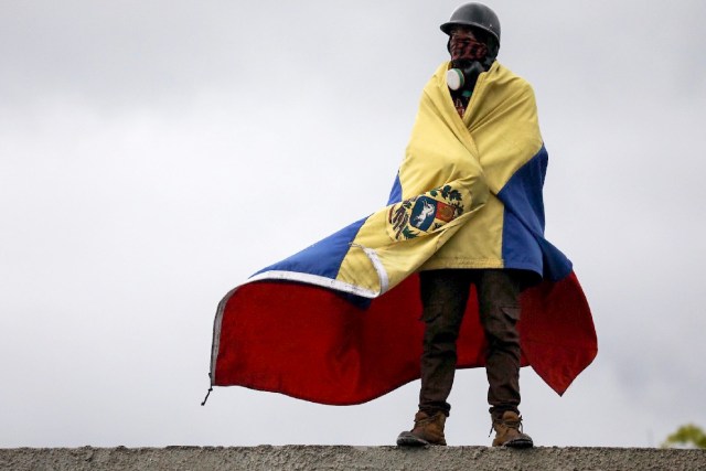 CAR23. CARACAS (VENEZUELA), 24/06/2017.- Un hombre que usa máscara de gas envuelve su cuerpo con una bandera venezolana durante una manifestación denominada "Venezuela le da un mensaje a la FAN (Fuerza Armada)" hoy, sábado 24 de junio de 2017, en Caracas (Venezuela). La oposición venezolana se moviliza hoy hasta las bases militares en Caracas y varios estados del país, mientras el chavismo marcha para conmemorar los 196 años de la Batalla de Carabobo, una acción militar decisiva en la independencia del país caribeño, y por el Día del Ejército Bolivariano. EFE/Miguel Gutiérrez