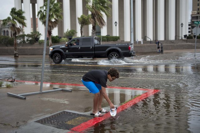 A child places a boat into a flooded road following the passage of Hurricane Harvey on August 26, 2017 in Galveston, Texas. / AFP PHOTO / Brendan Smialowski