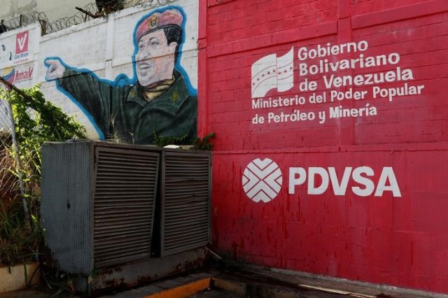 The logo of the Venezuelan state oil company PDVSA is seen next to a mural depicting Venezuela's late President Hugo Chavez at a gas station in Caracas, Venezuela March 2, 2017. Picture taken March 2, 2017. To match Insight VENEZUELA-INDIA/OIL REUTERS/Carlos Garcia Rawlins