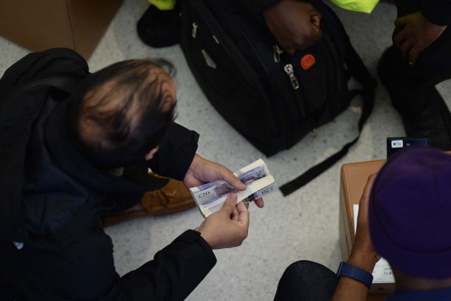 A customer holds a bundle of bank notes to pay for his Apple iPhone X after being one of the first to purchase the newly released smartphone at Apple's Regent Street store in central London on November 3, 2017. Apple's flagship iPhone X hit stores on November 3, as the world's most valuable company predicted bumper sales despite the handset's eye-watering price tag and celebrated a surge in profits. The device features facial recognition, cordless charging and an edge-to-edge screen made of organic light-emitting diodes used in high-end televisions. It marks the 10th anniversary of the first iPhone release and is released in about 50 markets around the world. / AFP PHOTO / CHRIS RATCLIFFE