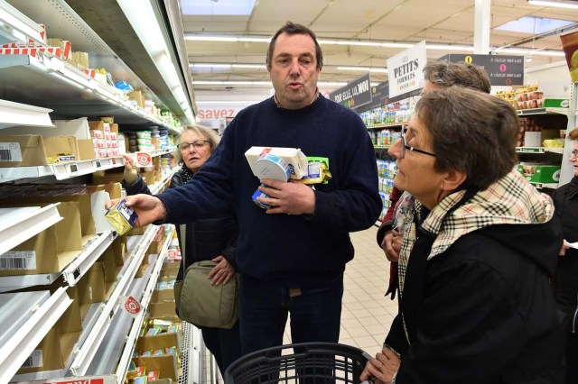 French farmer Ghislain De Viron (C) holds butter made from a blend of European Union milk as a substitute for French butter as he speaks to consummers in the hyper market Leclerc d'Alllonnes, near Le Mans, northwestern France, on November 10, 2017 during an action of French farmers to sell butter at a price that will remunerate them. / AFP PHOTO / JEAN-FRANCOIS MONIER