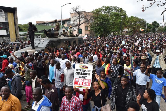 People march past an armoured personnel carrier towards the State House during a demonstration demanding the resignation of Zimbabwe's president on November 18, 2017 in Harare. Zimbabwe was set for more political turmoil November 18 with protests planned as veterans of the independence war, activists and ruling party leaders called publicly for President Robert Mugabe to be forced from office. / AFP PHOTO / -