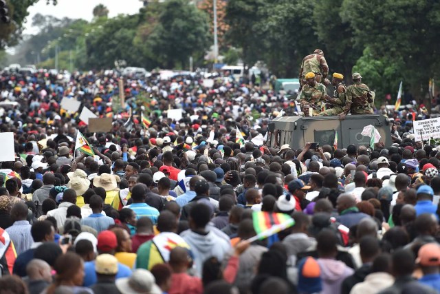 People march past an armoured personnel carrier towards the State House during a demonstration demanding the resignation of Zimbabwe's president on November 18, 2017 in Harare. Zimbabwe was set for more political turmoil November 18 with protests planned as veterans of the independence war, activists and ruling party leaders called publicly for President Robert Mugabe to be forced from office. / AFP PHOTO / -