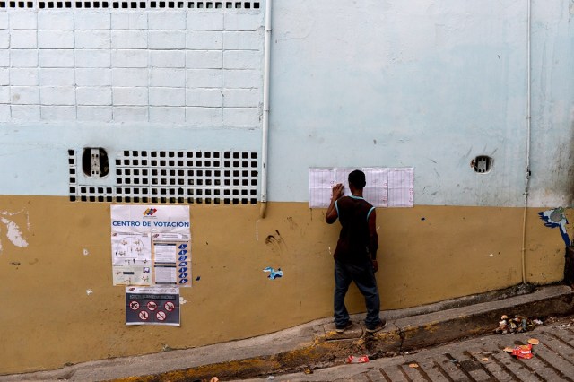 A man looks for his name on electoral rolls before voting in the municipal elections in Caracas on December 10, 2017. / AFP PHOTO / FEDERICO PARRA