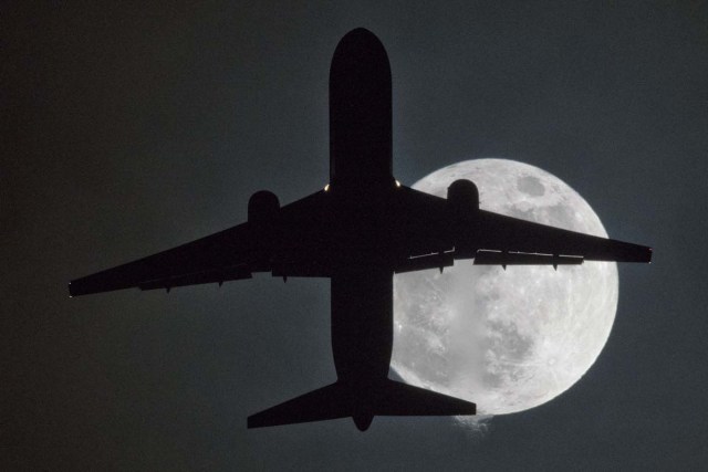 A plane flys in front of a "super moon" or "wolf moon" on its approach to London Heathrow Airport on January 1, 2018. / AFP PHOTO / Justin TALLIS