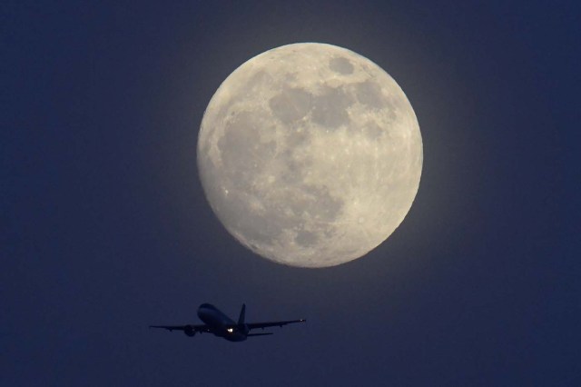 An aicraft flies infront of a full moon over London, Britain, January 30, 2018. REUTERS/Toby Melville