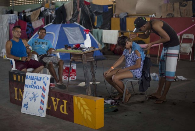 Venezuelan migrants have their hair cut by a fellow refugee, at a shelter in the city of Boa Vista, Roraima, Brazil, on February 24, 2018. When the Venezuelan migratory flow exploded in 2017 the city of Boa Vista, the capital of Roraima, 200 kilometres from the Venezuelan border, began to organise shelters as people started to settle in squares, parks and corners of this city of 330,000 inhabitants of which 10 percent is now Venezuelan. / AFP PHOTO / MAURO PIMENTEL