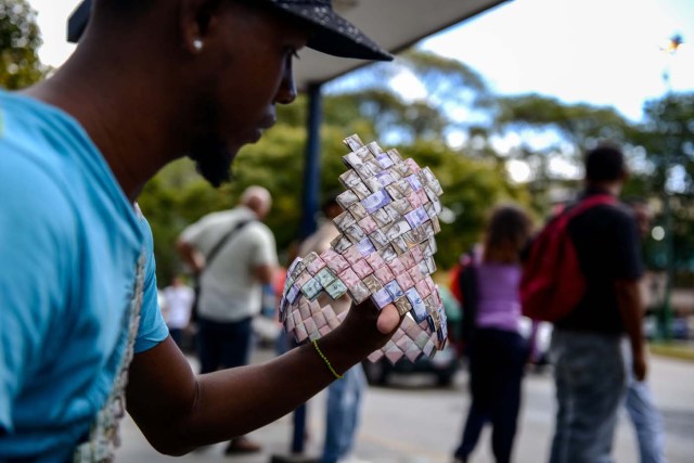 Wilmer Rojas, 25, shows a paper crown he sewn up, using Bolivar bills in Caracas, on January 30, 2018. A young Venezuelan tries to make a living out of devalued Bolivar banknotes by making crafts with them.  / AFP PHOTO / FEDERICO PARRA