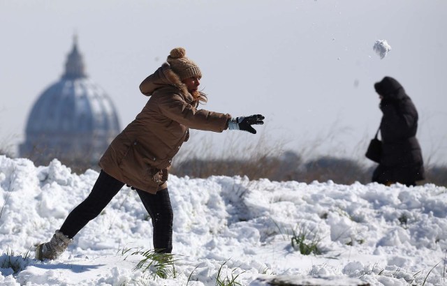 A woman throws a snowball as Saint Peter's Basilica dome is seen in the background after a heavy snowfall in Rome, Italy February 26, 2018. REUTERS/Alessandro Bianchi