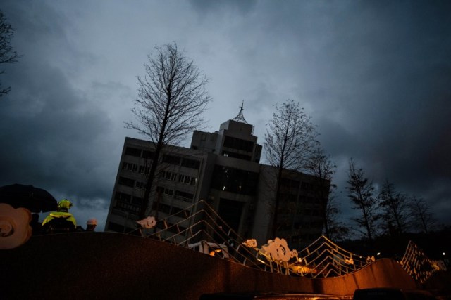 Los trabajadores de rescate (L) esperan mientras el edificio Yun Tsui (espalda) se inclina hacia un lado después de un terremoto durante la noche en la ciudad taiwanesa de Hualien el 7 de febrero de 2018. / AFP PHOTO / Anthony WALLACE