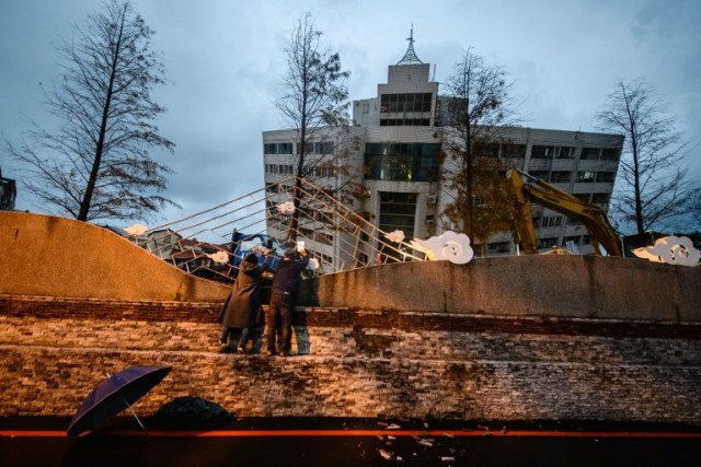 Los espectadores trepan una pared para tomar fotos del edificio Yun Tsui (espalda) mientras se inclina hacia un lado después de un terremoto en la ciudad taiwanesa de Hualien el 7 de febrero de 2018. / AFP PHOTO / Anthony WALLACE