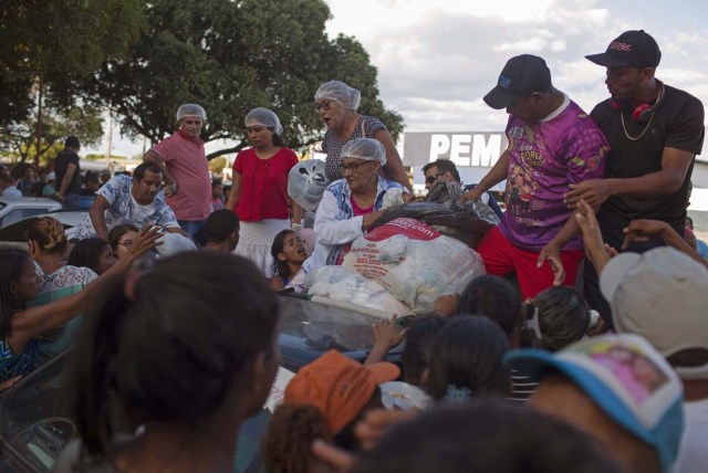 Los refugiados venezolanos se reúnen para recibir ropa distribuida por voluntarios en la plaza Simón Bolívar en la ciudad de Boa Vista, Roraima, Brasil, el 25 de febrero de 2018. Cuando el flujo migratorio venezolano estalló en 2017, la ciudad de Boa Vista, capital del estado de Roraima, a 200 kilómetros de la frontera con Venezuela, comenzó a establecer refugios a medida que la gente comenzaba a establecerse en plazas, parques y rincones de esta ciudad de 330,000 habitantes habitantes de los cuales el 10 por ciento es ahora venezolano. / AFP PHOTO / Mauro PIMENTEL