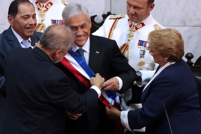 Chile's new President Sebastian Pinera (C) receives the presidential sash from Senate President Carlos Montes (L) while outgoing President Michelle Bachelet (R) helps them during the inauguration ceremony at the Congress in Valparaiso, Chile, on March 11, 2018. Rightwing billionaire businessman Pinera was sworn in as the new president of Chile for the second time. / AFP PHOTO / CLAUDIO REYES