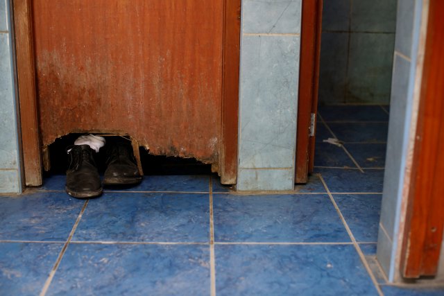 Los zapatos de Alvaro Betancourt, que viaja en autobús desde Caracas a Chile, se ven a través de un agujero en una puerta mientras toma una ducha en una estación de autobuses en Tumbes, Perú, el 11 de noviembre de 2017. Carlos García Rawlins: "En el terminal de autobuses en Tumbes el baño estaba en mal estado, los baños estaban sucios y no funcionaban correctamente, el piso y las paredes de las duchas estaban cubiertos de hongos, hasta el punto de que alguien colocó un pedazo de madera en el piso para que pudieran pararse bajo el agua sin tocar el piso. Pero después de varios días sin bañarse, las condiciones del baño no eran tan importantes, así que uno por uno, la mayoría de los viajeros tomaron una ducha antes de continuar en la carretera ". REUTERS / Carlos Garcia Rawlins