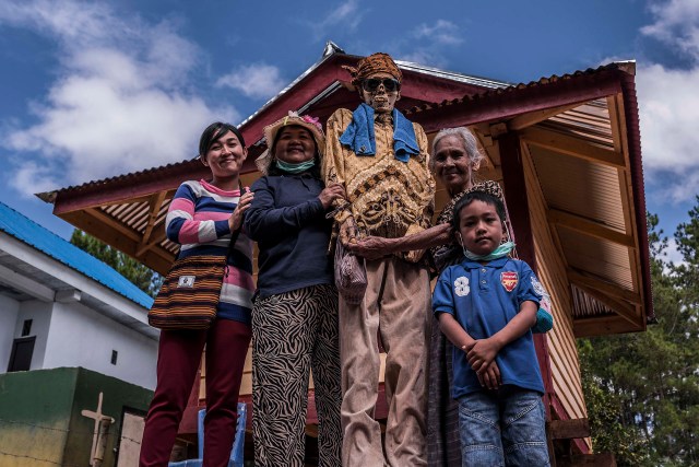 PIC BY Claudio Sieber / CATERS NEWS - (PICTURED people pose with a relative)THESE images show a unique insight into the village where the living dig up their dead relatives to clean their bones and to dress them up. The dead can even remain in homes for decades until the family throw a huge party in their honour. The corpses are treated as sick until they finally find peace after funeral rites known as Rambu Solo The bizarre ritual was pictured in South Sulawesi, Indonesia, where even buried relatives are taken out of their coffins for new outfits and a bone polish. SEE CATERS COPY