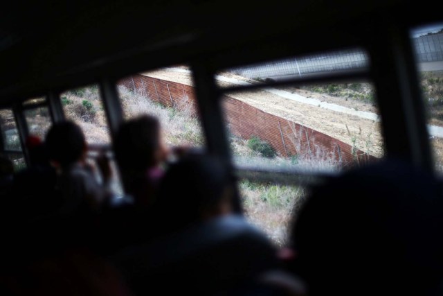 Members of a caravan of migrants from Central America ride on a bus past the border fence between Mexico and the U.S., to gather in a park prior to preparations for an asylum request in the U.S., in Tijuana, Mexico April 29, 2018. REUTERS/Edgard Garrido